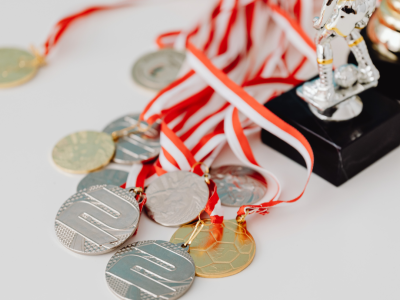 Uz balta fona redzamas sudraba un zelta medaļas ar sarkanbaltām lentēm