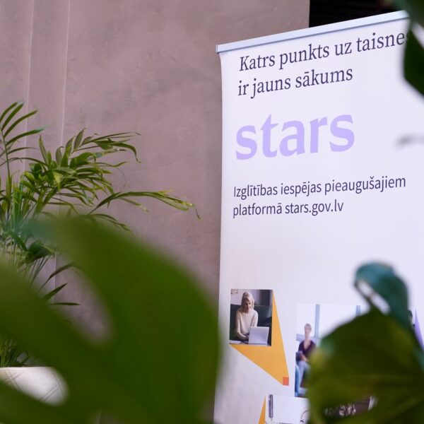 Balts stends ar tekstu "Katrs punkts uz taisnes ir jauns sākums", lieliem burtiem "stars" un "Izglītības iespējas pieaugušajiem platformā stars.gov.lv", redzams telpās starp zaļiem augiem.